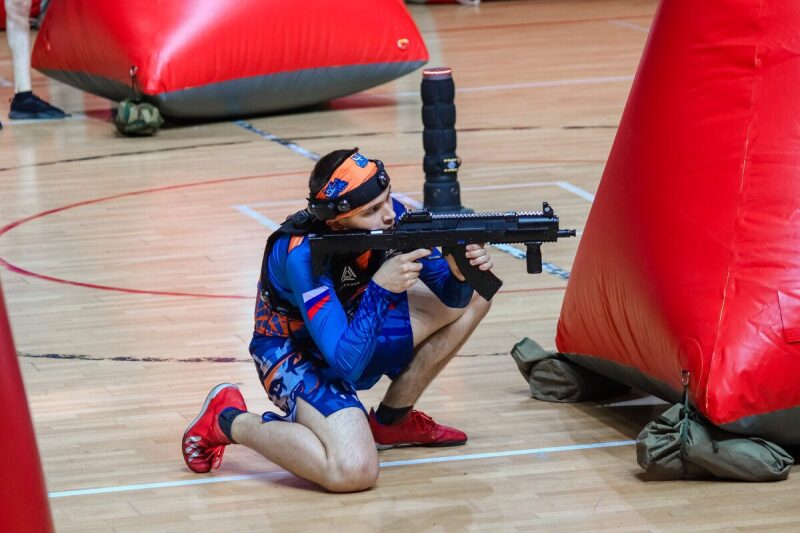 Боец LASERWAR в низкой стойке с оружием у красного препятствия